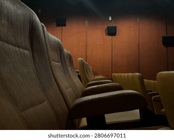 Low angle wide shot of empty rows of brown velvet seats inside a dim movie theater with dramatic wall lighting to create an atmospheric cinematic vibe before a film screening
