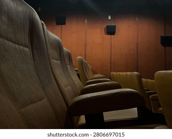 Low angle wide shot of empty rows of brown velvet seats inside a dim movie theater with dramatic wall lighting to create an atmospheric cinematic vibe before a film screening