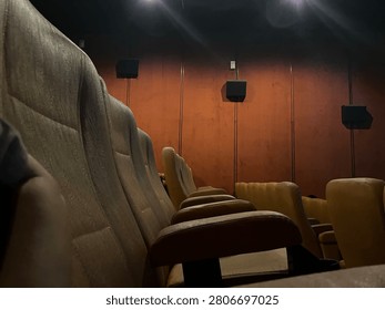 Low angle wide shot of empty rows of brown velvet seats inside a dim movie theater with dramatic wall lighting to create an atmospheric cinematic vibe before a film screening