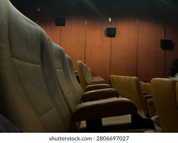 Low angle wide shot of empty rows of brown velvet seats inside a dim movie theater with dramatic wall lighting to create an atmospheric cinematic vibe before a film screening