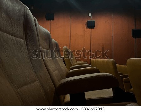 Low angle wide shot of empty rows of brown velvet seats inside a dim movie theater with dramatic wall lighting to create an atmospheric cinematic vibe before a film screening