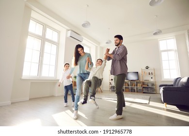 Low angle wide shot happy family with kids playing together at home. Young couple with little children enjoying free time and having fun in light spacious living-room of new house or rented apartment - Powered by Shutterstock