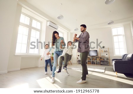 Low angle wide shot happy family with kids playing together at home. Young couple with little children enjoying free time and having fun in light spacious living-room of new house or rented apartment