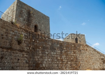 Low angle wide view of the massive stone walls, walkways and medieval towers of Montalegre Castle against a clear blue sky in Portugal.
