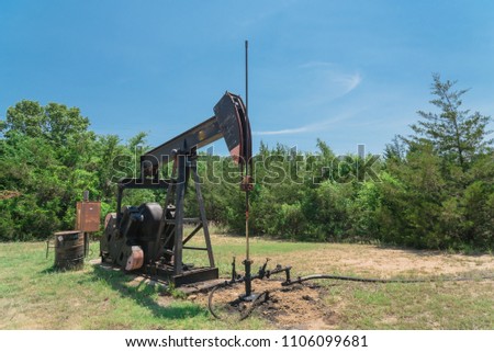 Low angle working pump jack fracking crude extraction machine. Pumping crude oil out of well to tank. Pumper, water emulsion at oil drilling site in Gainesville, TX, US. Energy, Industrial background