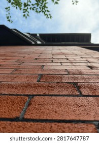 Low angle worm's eye perspective of red brick wall rising up towards sky and roof with tree leaves framing the top