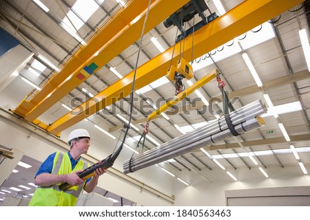 Low angled shot of a technician wearing a helmet while operating hoist with raw aluminum in a hi-tech manufacturing plant.