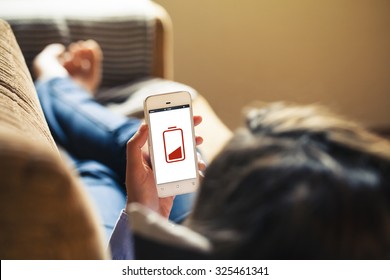 Low Battery Concept. Woman Holding A Mobile Phone While Lying On The Sofa At Home.