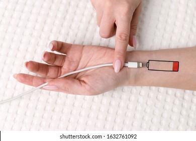 Low battery symbol drawn on human hand. Tired woman lying on the bed, trying to charge from USB, holding cable with your finger. Overwork, exhausted, chronic fatigue, living energy concept.  - Shutterstock ID 1632761092