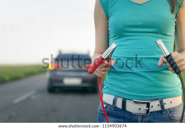 Low car battery charge. Need\
recharging. Driver holding a automobile cable starter in the\
hands.