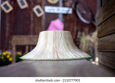 A low close-up view, an antique wicker hat made of palm leaves rests on a wooden chair set within an old wooden room of a house in rural Thailand.