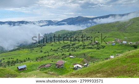 Low clouds drift across rolling alpine meadows and remote mountain hamlets in the highlands of Adjara, Georgia. Dramatic fog, green hills and rugged Caucasus peaks create a mysterious landscape.