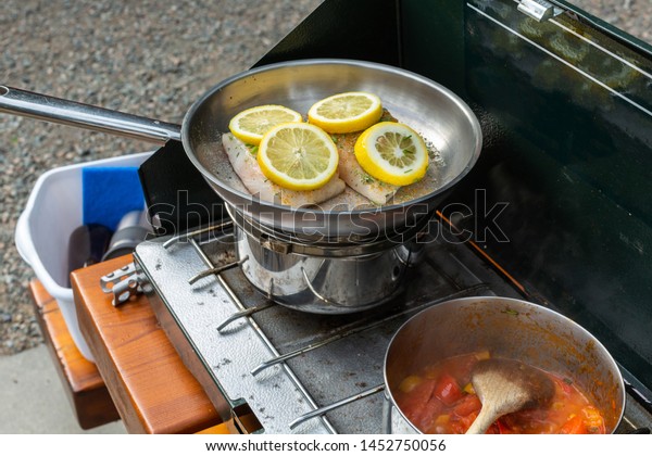 A low FOOD Map dinner of halibut with lemon slices\
and stewed tomatoes and red peppers cooks on a camp stove on a\
camping trip.