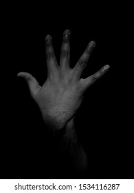 Low Key Black And White Photo Of A Man Showing The Back Of His Hand With His Fingers Sticking Out To Show The Number Five On A Plain Black Background