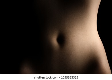 Low-Key-Bodyscape-Bild von Bauch und Hüften einer Frau auf schwarzem Hintergrund