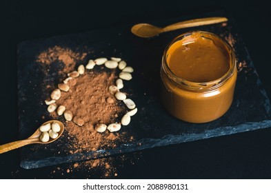 Low Key High Contrast Carob, Cocoa Peanut Butter Jar With Heart From Peanuts On A Black Stone Slate And Black Background