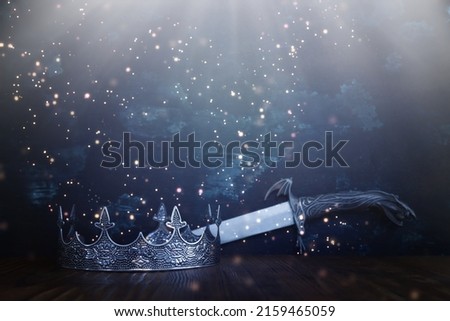 low key image of beautiful queen or king crown next to sword. fantasy medieval period. Selective focus