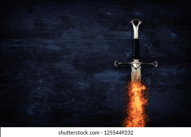 low key image of silver sword in the flames of fire. fantasy medieval period