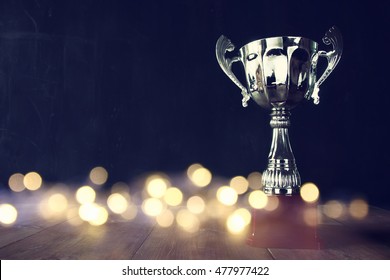 low key image of trophy over wooden table and dark background, with abstract shiny lights - Shutterstock ID 477977422