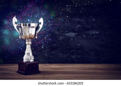 low key image of trophy over wooden table and dark background, with abstract glitter lights