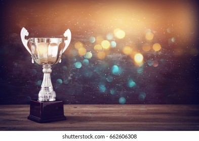 low key image of trophy over wooden table and dark background, with abstract glitter lights - Powered by Shutterstock