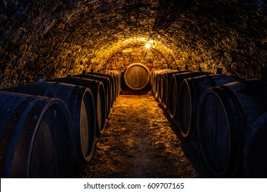 Low key image of a wine cellar with barrels around the walls and a single light bulb illuminating them.