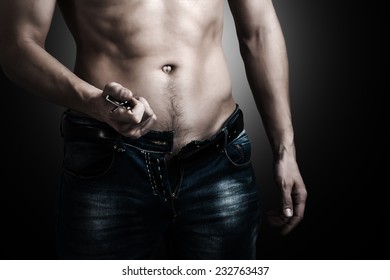 Low key. Man showing his muscular body. Stripper unzips jeans and belt.