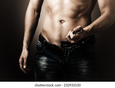 Low key. Man showing his muscular body. Stripper unzips jeans and belt