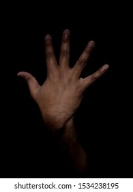 Low Key Photo Of A Brown Man Showing The Back Of His Hand With His Fingers Sticking Out To Show The Number Five On A Plain Black Background