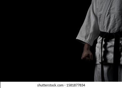 A low key photo of a half man in Aikido uniform with a strong fist keeping a martial arts pose.