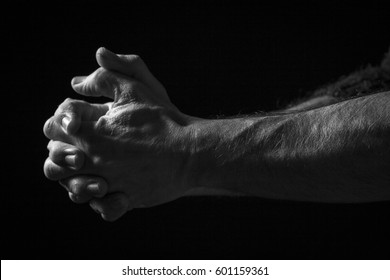 Low key portrait of hands in praying position. Black background