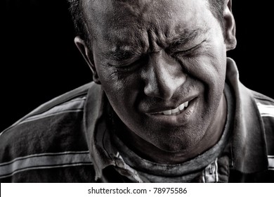 Low Key Portrait Of A Man Suffering From Extreme Anguish Pain Or Other Hardship Over A Black Background.