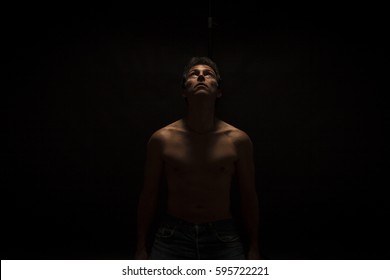 Low key portrait of shirtless handsome caucasian man, looking up. Black background