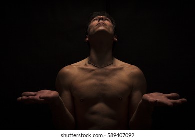 Low key portrait of shirtless man in Yoga position. Black background