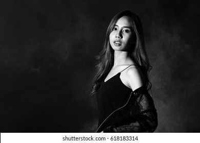 Low Key Portrait Of Tan Skin Asian Slim Healthy Woman In Black Background With Fog Smoke And Light From Back, Sexy Pose S Curve With Short Pants And Shadow, Black And White Color Concept