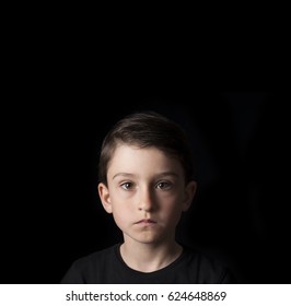 Low Key Portrait Of Young Boy Isolated On Black Background. Plenty Of Space Left For Copy. For Flyers, Posters And Other Commercial Purposes. Serious Face