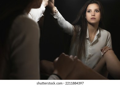 Low Key Portrait Of Young Woman Looking At Her Reflection In The Mirror In A Beam Of Light. Horizontally. 