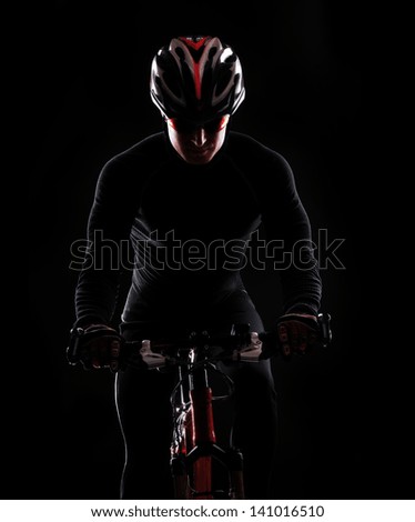 low key silhouette of a male cyclist riding his bicycle isolated on black