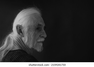 Low Key Studio Black And White Portrait Of Beautiful Gray Hair Old Man Looking Over His Shoulder At The Camera. Horizontally.