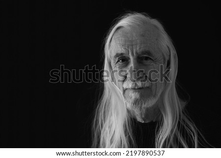 Low key studio  black and white portrait of smiling attractive old man with loose long gray hair. Horizontally. 