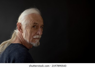 Low Key Studio  Portrait Of Beautiful Old Man With Gray Hair In A Braid Looking Over His Shoulder At The Camera. Horizontally.