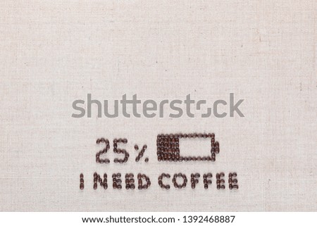 Low level battery with 'I need coffee' sign made from roasted coffee beans on creamy linen canvas, shot from above, aligned bottom center.