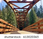 Low level view across Tioga Bridge includes wooden arch above bridge and evergreen forest in background. This bridge on North Umpqua River in Oregon gives hikers new access to a popular trail.