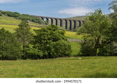 Low level view of Denthead viaduct on the famous Settle-Carlisle railway line through north Yorkshire and Cumbria in England, UK with old fashioned hay meadow and trees in the foreground. - Shutterstock ID 1994570171