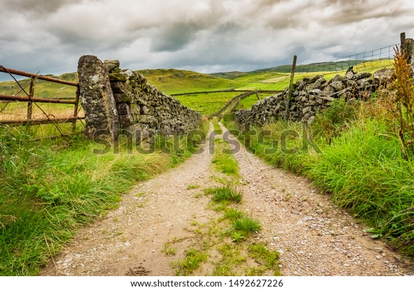 Low level view of a old dirt track\
leading to a valley in the Yorkshire Dales. Either side of the road\
is old, dry stone walling used for livestock\
containment.