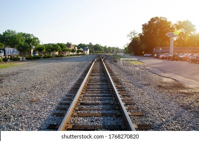 A low level view of a single track freight railway line leading straight into the distance, on the the edge of a small South Carolina town. The sun has just risen giving an orange glow to the right of