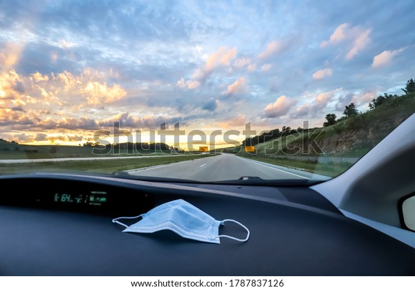 Low light image of\
a disposable mask sitting on a car\'s dashboard at sunset on the\
highway.  A roadtrip during the pandemic.  Shallow focus on mask,\
dashboard has texture.