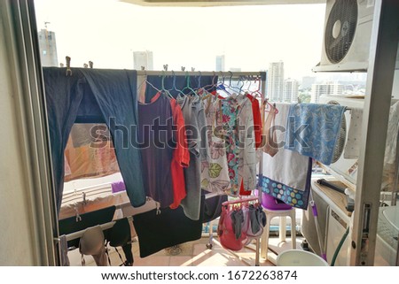 low light, soft shot of colorful washed household clothes remaining not dried on stainless steel rail at urban condominium balcony on rainy day. Background is city high rise. 