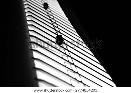 Low light through window blinds casts narrow shadows across a quiet interior, reflecting nightshift fatigue, isolation, and a subdued depressive mood.