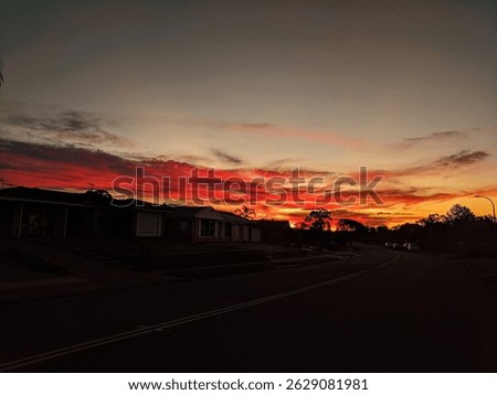 Low lying whispy clouds over a suburban street turn a bright crimson hue at sunset.